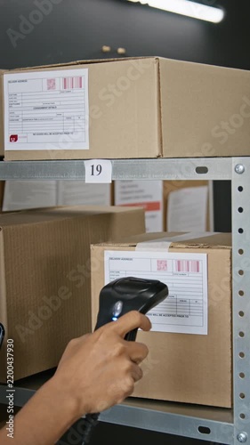 Vertical video of unrecognizable worker scanning barcodes on cardboard parcels with laser scanner for inventory tracking. Clip ideal for logistics, supply chain, and retail business promos
