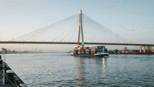 Modern cable-stayed bridge spanning a river with a cargo ship passing underneath