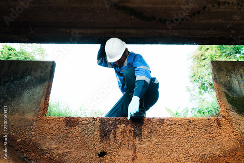 Worker in hard hat inspecting concrete drainage infrastructure, civil engineering site maintenance, professional technical evaluation.