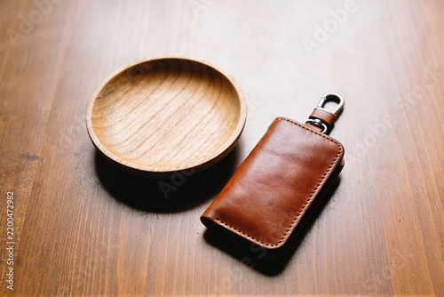 Brown leather key fob with a metal clip beside a shallow wooden bowl