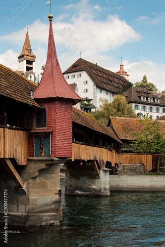 Foto Covered Wooden Bridge and Red Tower Beneath Historic Hillside Rooflines
