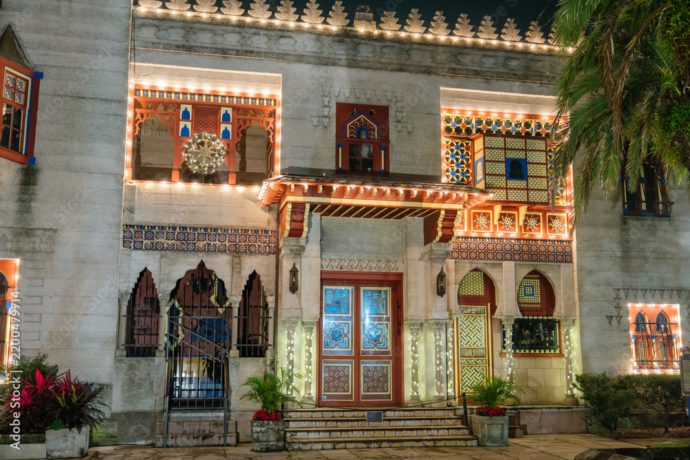 Obraz premium The entrance of Villa Museum features colorful Moorish arches, mosaic tiles, and geometric patterns. White Christmas lights and a glowing wreath illuminate the historic St. Augustine landmark at night