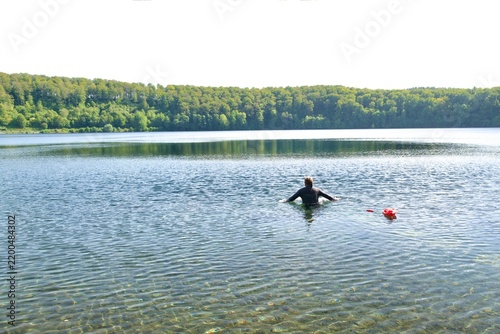 Open water swimmer in wetsuit with safety buoy swimming in a scenic lake
