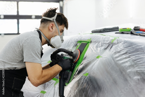 Фотография Automotive worker sanding car body with orbital sander and safety gear in bright