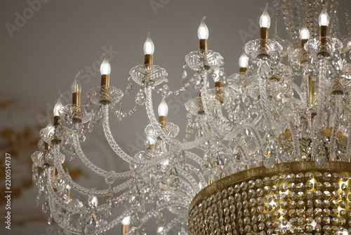 Warm incandescent light from ornate crystal chandelier fills luxury interior ceiling view, with curving glass arms and hanging crystal beads around gold beaded crown.