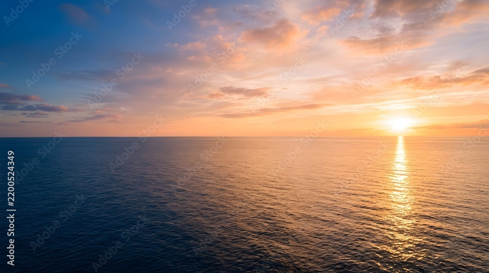 Fototapeta premium Vast calm blue ocean water meeting pastel golden sunrise horizon with soft clouds and sunbeams reflecting on gentle sea ripples.