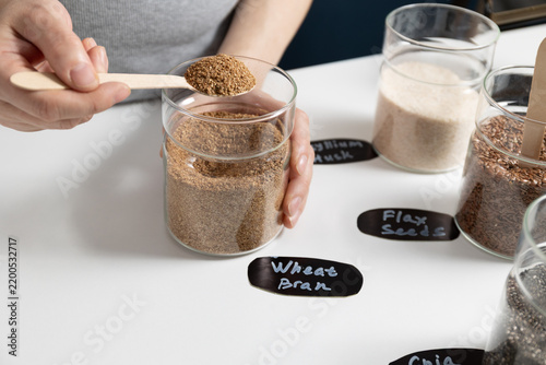Close-up of bran powder being scooped from a glass jar with a wooden spoon in a home kitchen