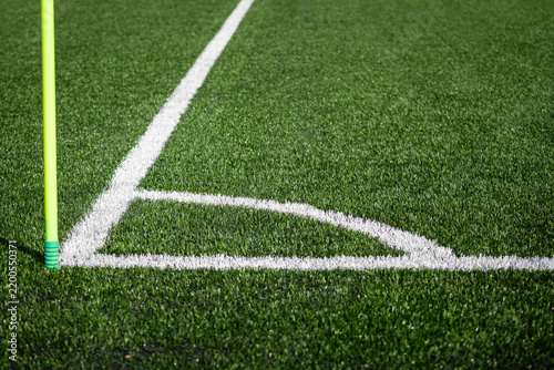 Corner of a soccer field with yellow corner flag and white markings on green artificial grass, close-up of football pitch.