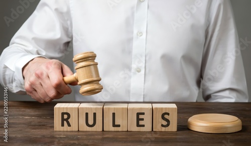 Judge holding a wooden gavel above wooden blocks with the word rules, concept of law and justice