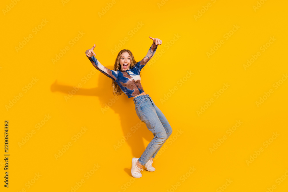 Obraz premium Young woman in casual outfit jumps with joy against a bright yellow background for lifestyle fashion advertising and promotion