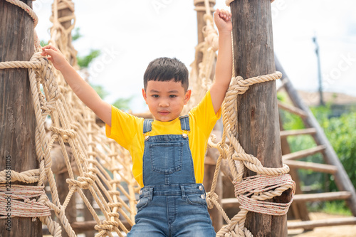A joyful child in a bright yellow shirt climbs a rope structure, showcasing the joy of play and outdoor adventure. Perfect for capturing childhood happiness.