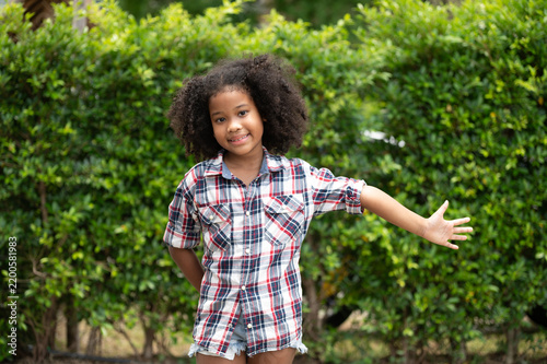 Bild auf Leinwand A joyful young girl with curly hair poses playfully outdoors amidst lush greenery, embodying innocence and freedom in nature's embrace