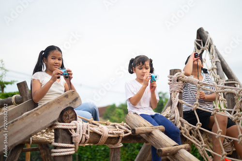 фотографія Three children enjoy playtime at a playground, capturing moments with toy cameras while sitting on wooden structures surrounded by greenery