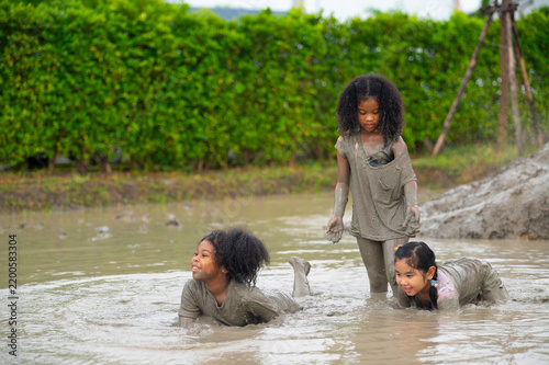Fotografía Three joyful children playfully splashing in muddy water, enjoying a carefree moment in nature, showcasing fun and laughter in an outdoor setting
