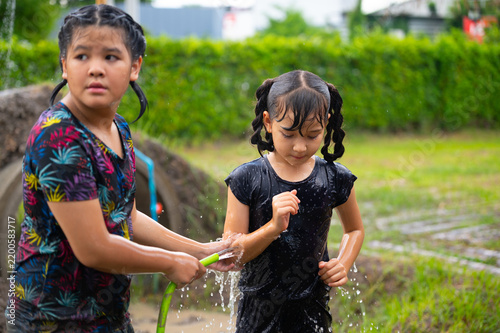 Two girls joyfully play with water in a lush garden, showcasing the happiness of childhood and the beauty of outdoor activities during a sunny day.