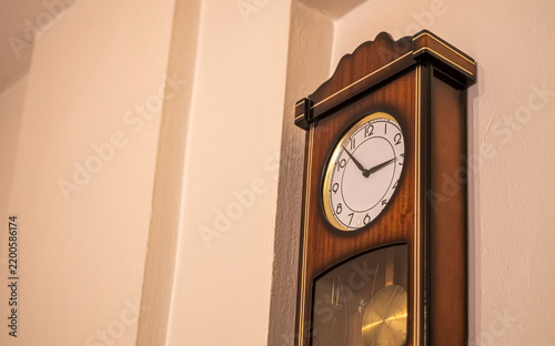 Vintage wooden pendulum wall clock with gold bezel mounted in a home interior corner. Use for home decor, interior design, lifestyle, and real estate content.