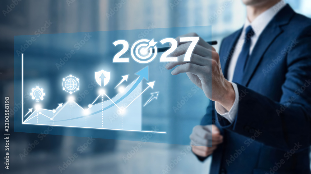 Obraz premium Businessman drawing 2027 target over glowing business growth graph