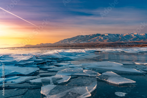 View of ice shove pile along the shoreline of Utah Lake at sunrise with snow-capped mountains in the background under a colorful sky in Saratoga Springs, Utah, United States.