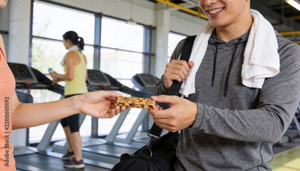 Fototapeta premium Receiving male reaching for granola bar at fitness center with towel and duffel bag, copy space