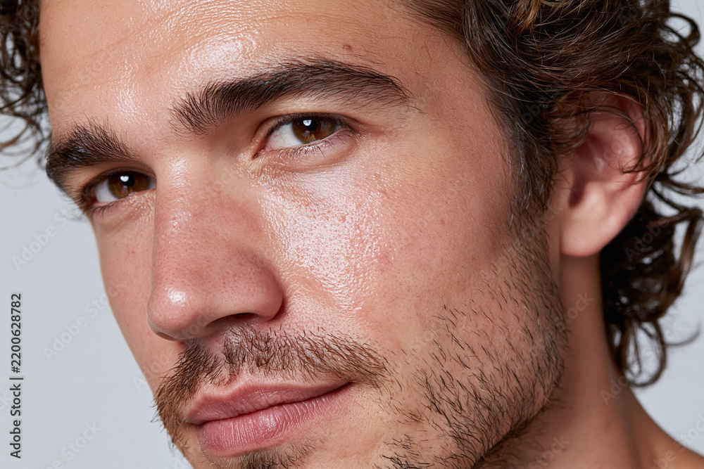 Fototapeta premium Close up portrait of man with dewy skin, stubble, brown eyes, and textured cheek expressing calm confidence