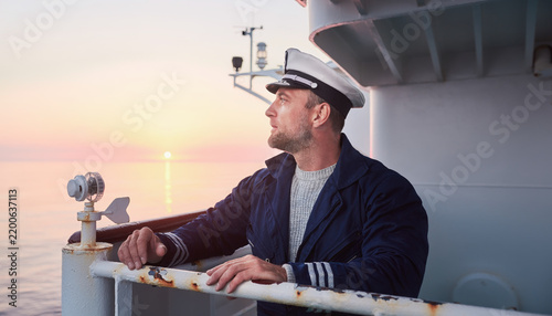 A sailor on a ship deck gazing at the sunset horizon.