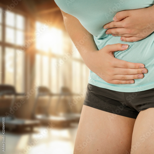 Woman stretching and massaging painful body areas of stomach– muscle pain and health concept.