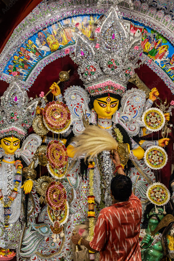Fototapeta premium Traditional Bengali Durga Puja Idol with hindu priest performing aarti rituals to Goddess Durga during religious festival.