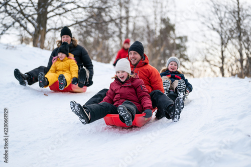 Smiling family enjoying winter sledding down snowy hill together