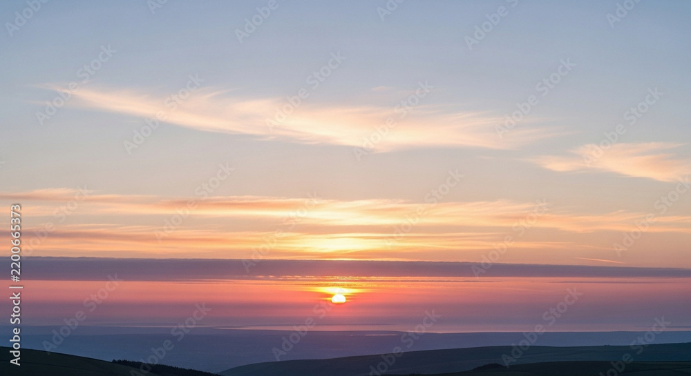 Fototapeta premium Breathtaking panoramic view of the sun setting over rolling hills casting a warm orange glow across the dramatic evening sky filled with soft clouds creating a peaceful atmosphere