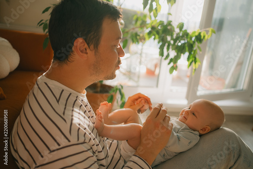 Father holding his happy newborn baby on his lap, looking at the child with affection, strengthening their bond during a tender family moment in the light filled home