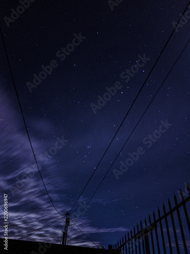 Fotografie Líneas de alta tensión bajo un cielo nocturno profundo con nubes tenues y estrellas sutiles