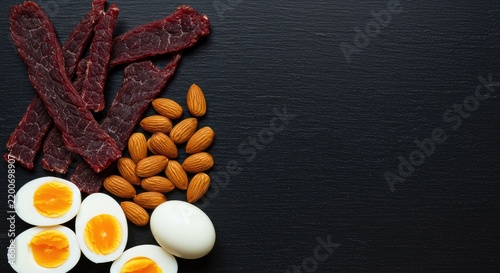 Flat lay of healthy protein sources with jerky, almonds, and hard-boiled eggs on dark background