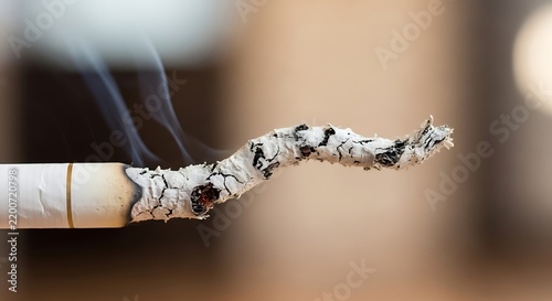 Close-up of a burning cigarette with ash and smoke in indoor setting