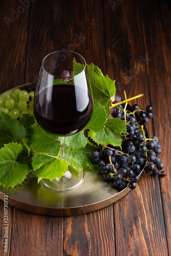 Obraz na płótnie Glass of red wine with fresh green and dark grapes on a metal tray