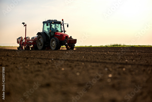 Farmer driving tractor with seeder attachment in a freshly cultivated field