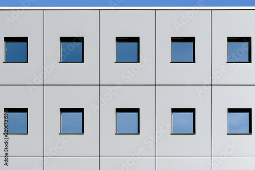 Minimalist white building facade with irregularly spaced square windows showing sky reflections. Clean, modern, geometric architecture.