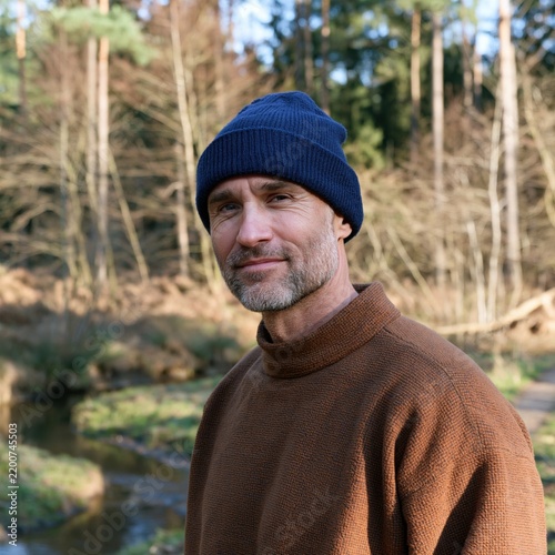 Outdoor autumn portrait of a thoughtful man wearing a navy beanie near a woodland creek for lifestyle profile and background banner design