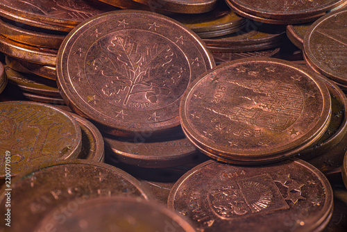 Closeup of overlapping copper colored euro cent coins showing embossed national designs, stars, numbers, worn metallic surfaces, and detailed circular edges in a coin pile
