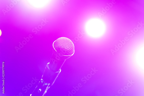 Close up of a live vocal microphone mounted on a stage stand against a vibrant glowing purple background with bright spotlights illuminating the venue.