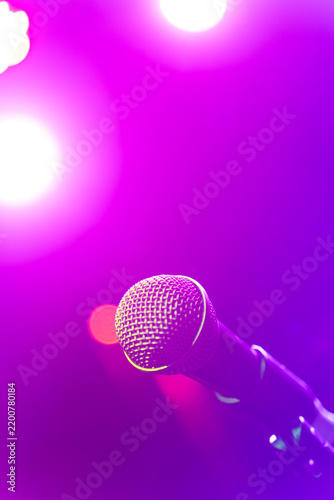 Close up of a live vocal microphone mounted on a stage stand against a vibrant glowing purple background with bright spotlights illuminating the venue.