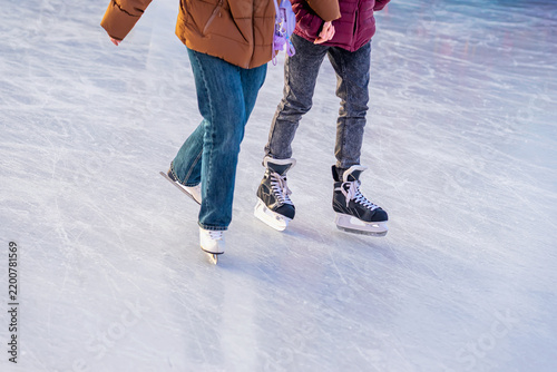 Two People Ice Skating Together on Winter Rink. Cropped view of two people skating together across outdoor ice rink. Ice skates, casual winter clothing, frozen surface illustrate seasonal recreation