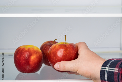 Hand picking fresh red apple from group in fridge