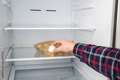 Hand taking the last egg from carton in empty fridge