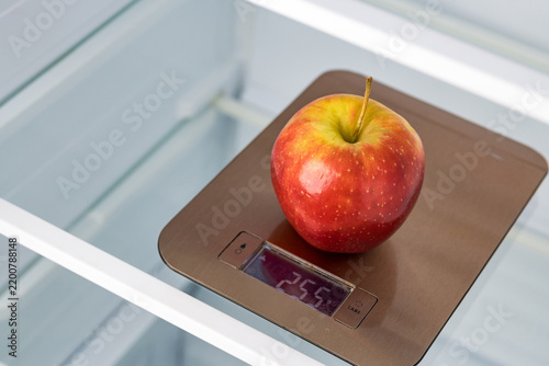 Apple weighing on kitchen scales in empty refrigerator
