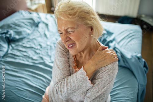 Senior woman wincing with shoulder pain in bedroom