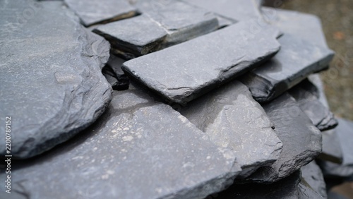Stack of dark gray natural slate roofing tiles showing rough textured surface and raw layered edges in a close up view