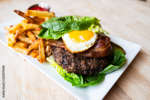Gluten free lettuce wrapped breakfast burger with a sunny side up egg, bacon, and delicious crispy french fries on the side from a popular restaurant and bar.