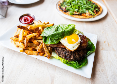 Gluten free lettuce wrapped breakfast burger with a sunny side up egg, bacon, and delicious crispy french fries on the side from a popular restaurant and bar.