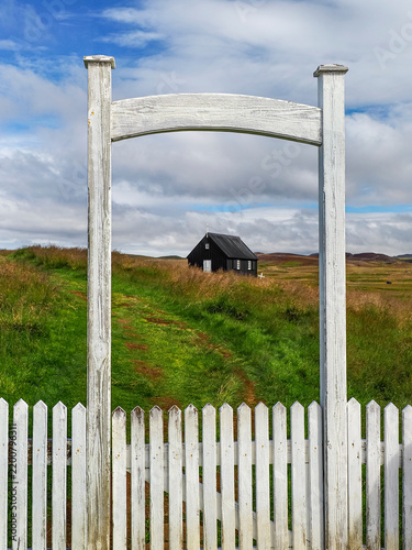 White wooden fence in the foreground and small black church visible in the distance. Krýsuvík or Krísuvíkurkirkja church in the Reykjanes Peninsula, Iceland. Symbol of heritage Icelandic identity.