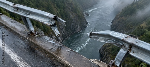 Bent steel bridge guardrail above a river gorge with a torn gap and twisted posts
